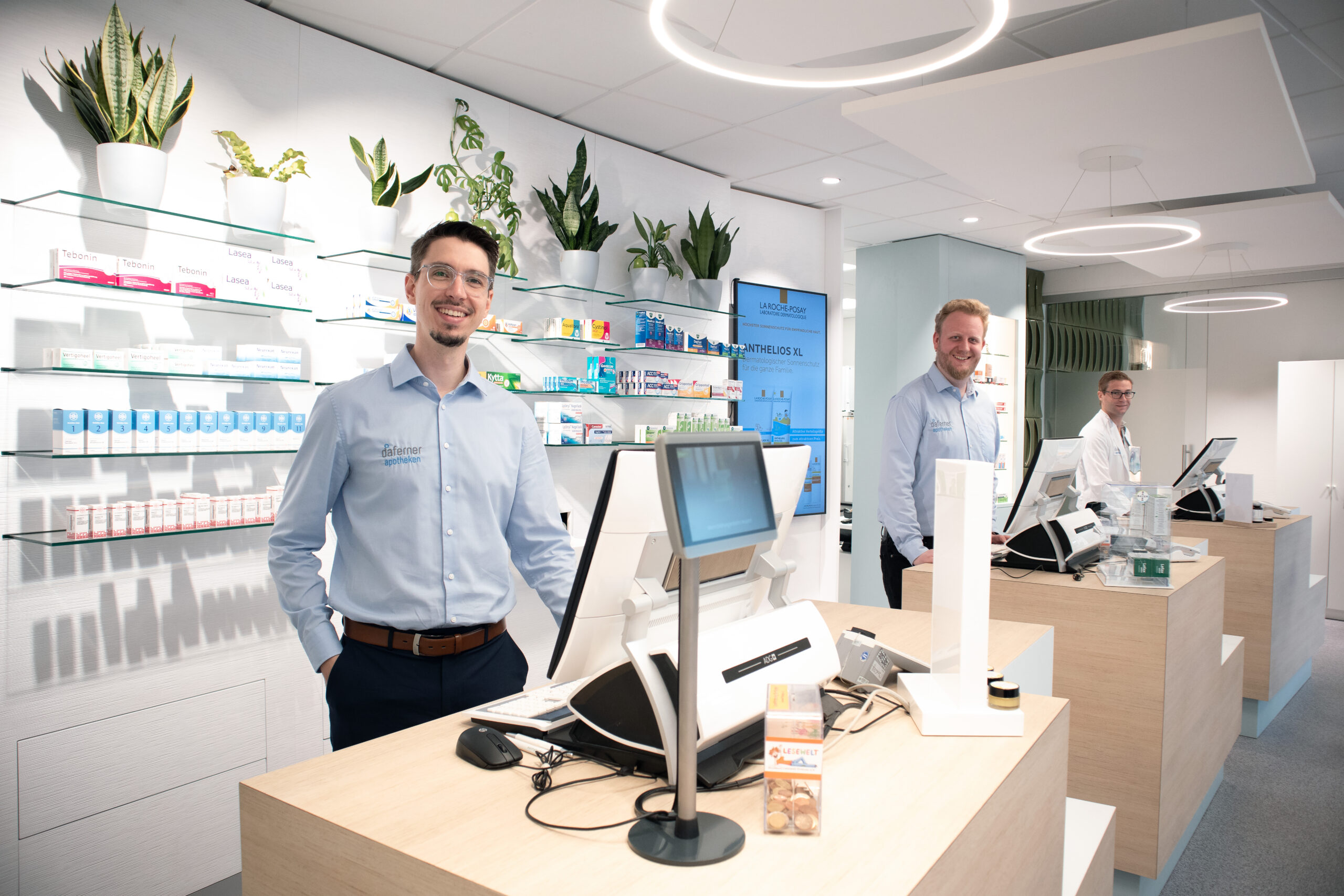 Yannick-Sebastian-Florian_anderkasse_edited_LR_PS Drei Apotheker stehen hinter den Kassen einer modernen Apotheke.
